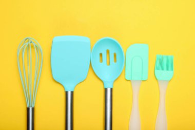 Mutfak gereçleri seti: mutfak fırçası, çırpma teli, sarı arka plan üzerinde spatula. Üstgörünüm, minimalis