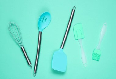 Mutfak aletleri seti: mutfak fırçası, çırpma teli, mavi arka plan üzerine spatula. Üstgörünüm, minimalis