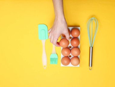 Kadın eli sarı arka plandaki yumurta tepsisinden tavuk yumurtası alıyor. Mutfak konsepti, mutfak silikon aracı, minimalizm