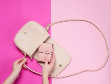 Kadın el pastel arka plan üzerinde bir çanta bir deri cüzdan alır. Üst görünüm, düz yatıyordu, minimalizm