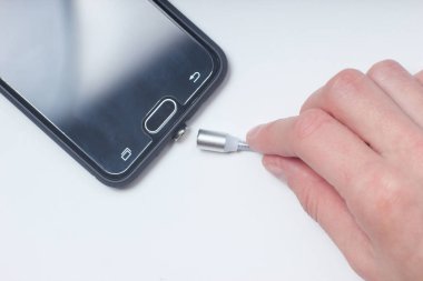 İnsanın eli, akıllı telefonu beyaz bir arka plan üzerinde şarj etmek için manyetik kabloyu bağlar. Üstte görüntü.