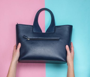 Kadın elleri renkli bir kağıt arka plan üzerinde bir deri çanta tutun, üst görünümü, minimalizm