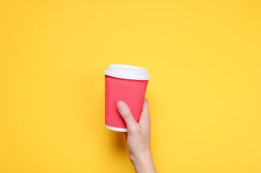 Kadın el sarı kağıt arka plan üzerinde kırmızı kağıt kahve fincanı tutan. Üst te. Minimalizm