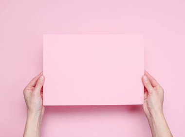 Kadın elleri pembe arka plan üzerinde pembe kağıt levha tutan. Üst te. Mockup, kopyalama alanı, minimalizm