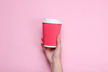 Kadın el pembe pastel arka plan üzerinde kırmızı kağıt kahve fincanı tutan. Üst te. Minimalizm