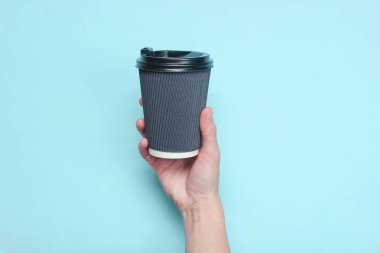Kadın el mavi pastel arka plan üzerinde siyah kağıt kahve konteyner tutan. Üst te. Minimalizm