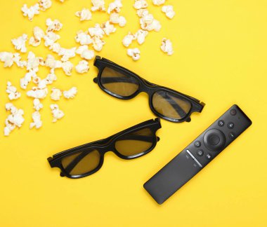 İki çift 3d gözlük, Tv uzaktan kumandası, sarı arka plan üzerinde patlamış mısır. Üst görünüm, düz yatıyordu