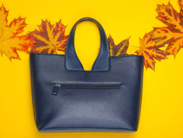 Autumn collection. Leather bag of fallen autumn leaves on a yellow background. Seasonal accessories. Top view. Copy spac