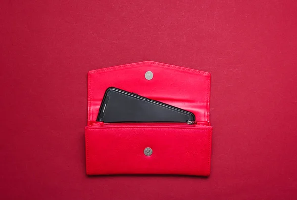 Smartphone in a red leather wallet on red background. Top vie