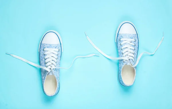 Fashionable sneakers with untied laces on a blue background. Top view, minimalism