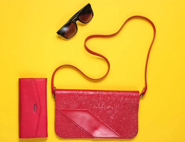 Retro style red leather bag, wallet and sunglasses on yellow background, top view