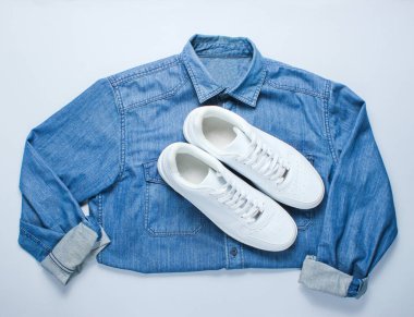 Gri arka planda denim gömlek ile düz yatıyordu tarzı beyaz hipster Sneakers. Retro kültür, üst görünüm