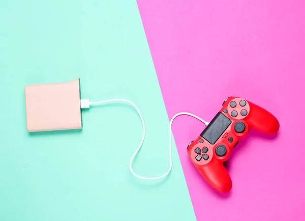 現代の赤いプラスチックのゲームパッドは 色付きのネオンの背景にパワーバンクから充電されています トップビュー ミニマリス — ストック写真