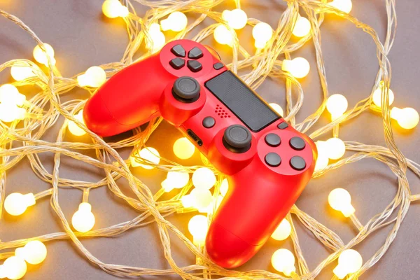 Red gamepad among glowing bright garlands on gray background. Minimalis