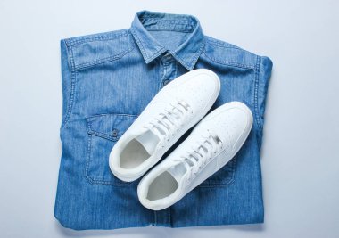Gri arka planda denim gömlek ile düz yatıyordu tarzı beyaz hipster Sneakers. Retro kültür, üst görünüm