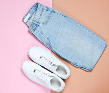 Pastel arka planda mavi moda kot pantolon ve beyaz hipster spor ayakkabıları. Üst görünüm, minimalizm