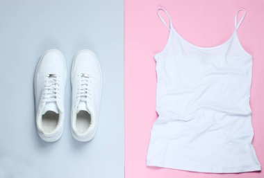 Beyaz kadın tişörtü, pembe-gri pastel arka planda beyaz hippi ayakkabıları. Üst manzara, düz yatış, minimalizm