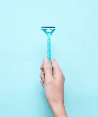 Kadın el mavi bir arka plan üzerinde epilasyon için jilet tutan. Üst görünüm, minimalizm, düz yatıyordu stil