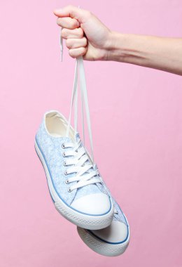 El pembe pastel arka plan üzerinde ayakkabı bağcıkları retro tarzı hipster spor ayakkabıları tarafından tutar. Minimalis