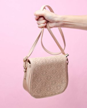 Kadın el pembe pastel arka plan üzerinde kayış deri moda çanta tutan. Minimalis