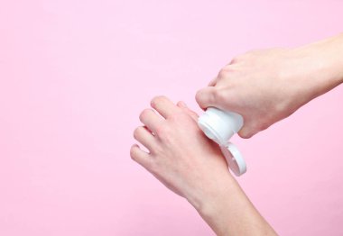 El bakımı. Kadın krem tüp tutan ve pembe pastel arka plan üzerinde yumuşak el cilt için onu güzel ellerine nemlendirici krem uygulayarak. Üst görünüm, minimalizm, düz yatıyordu