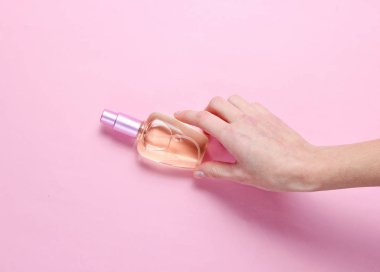Kadın el pembe pastel arka plan üzerinde parfüm şişesi alır. Minimalizm. Güzellik ve moda konsepti. Üstte görüntü