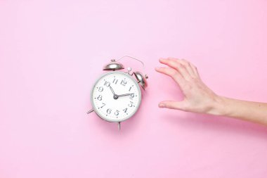 Kadın el pembe arka plan üzerinde çalar saat alır. Üst te. Uyanma zamanı. Minimalis