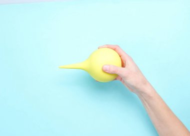 Kadın el mavi arka plan üzerinde sarı tıbbi enema tutar. Üstgörünüm, minimalis