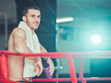 Boynunda havlu ve elinde su şişesi ile Boxer adam gülümseme ve halka köşesinde istirahat. Dinlenme konsepti