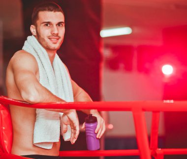 Boynunda havlu ve elinde su şişesi ile Boxer adam gülümseme ve halka köşesinde istirahat. Dinlenme konsepti