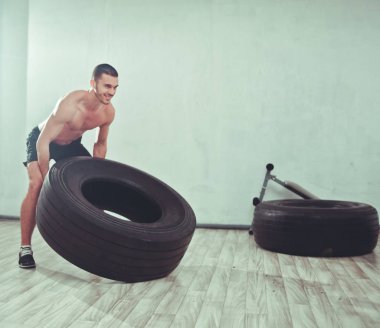 Young sports man raises a large weight wheel. training process. Functional training, workou