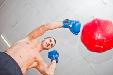 Yakışıklı spor adam boksör bir kum torbası ile el yumrukları trenler. Alt görünüm.