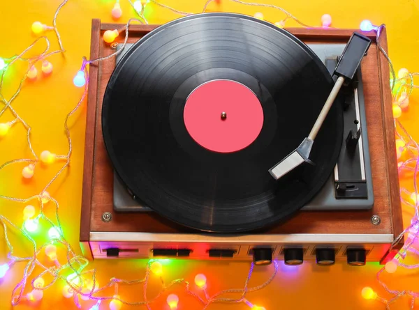 Retro 80s vinyl player with bright glowing garlands on a yellow background. Top view, minimalism