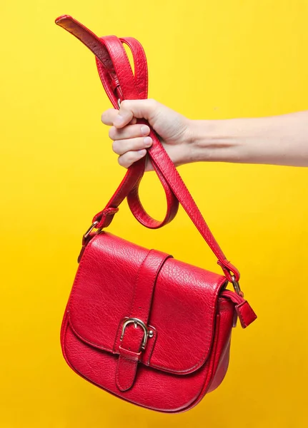 Kadın el sarı bir arka plan üzerinde kayış tarafından kırmızı deri çanta tutan. Minimalis