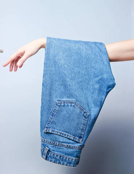 Calça Jeans Azul Pendurada Uma Mão Feminina Fundo Cinza Concurso — Fotografia de Stock