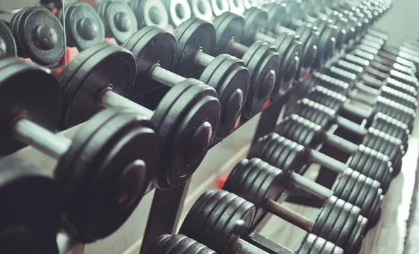 Close up many metal dumbbells on rack in sport fitness center. Black dumbbell set.