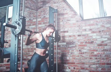 Atletik genç kadın demirci makinesiyle jimnastik salonunda pencereli tuğladan duvara doğru hamle yapıyor. Tonlanmış resim