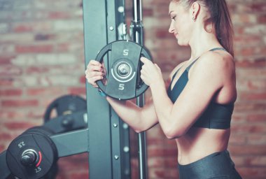 Fitness kadın spor salonunda tuğla duvara karşı barbell ağırlık diskkoyarak