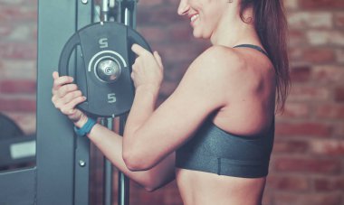 Çekim atletik kadın spor salonunda tuğla duvara karşı halter ağırlık disk koyarak güleryüzlü