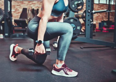 Spor salonunda dambıllarla spor vücut egzersizi yapan bir kadın. Dambıllarla saldırıyor. Eğitim kavramı