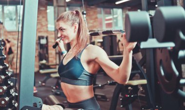 Spor salonunda sırtını, kollarını ve omuzlarını egzersiz makinesiyle çalıştıran bir sporcu kadın.