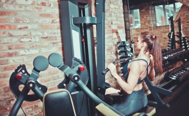 Spor salonunda, spor konseptinde, spor salonunda, spor salonunda sırtını ağırlık makinesiyle çalıştıran sportif bir kadın.