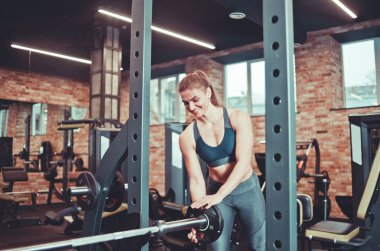 Sporcu kadın spor salonunda halter takıyor.