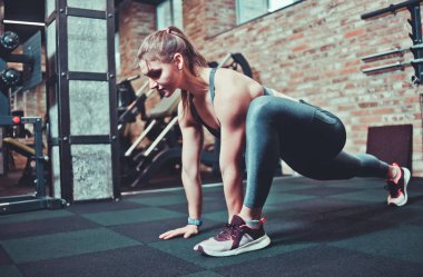 Spor kıyafetleri içinde mükemmel vücudu olan atletik genç bir kadın spor salonunda bacaklarını esnetiyor. Trenden önce ısın.