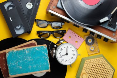 Retro öznitelikleri, 80'lerin medyası. Vinil çalar, video kasetleri, ses kasetleri, 3d gözlük, kayıtlar, radyo, vintage çalar saat, sarı arka plan üzerinde eski kitaplar. Üstte görüntü