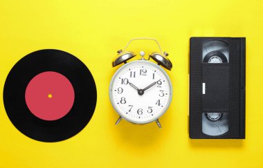 Retro vinil kayıt, eski çalar saat, sarı arka plan üzerinde video kaset. 80s. Üst görünüm. Minimalizm