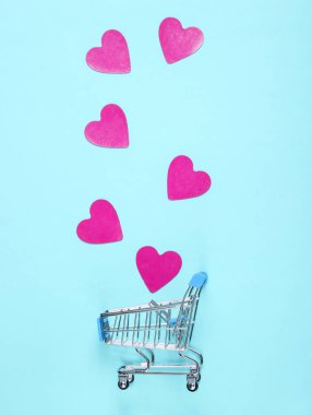 Mini alışveriş arabası, mavi pastel arka plan üzerinde dekoratif kalpler, üst görünümü, minimalizm. Kavramsal fotoğraf