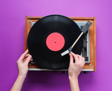 Kadın eli, mor arka planda plakası olan retro vinil plak çalar kuruyor. Üst görünüm