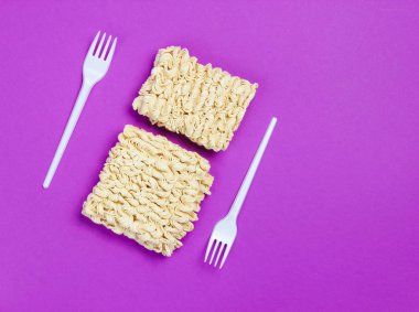 Mor arka planda çiğ erişte ve plastik çatal, minimalizm. Üstte görüntü