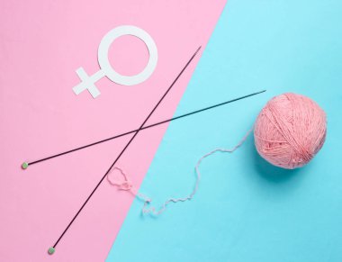 Kadınların hobisi. Örgü iğneleri, iplik yumağı, pastel arka planda dişi cinsiyet sembolü. Üst görünüm, minimalizm